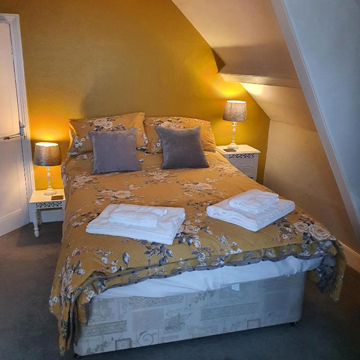 B&B in Little Haven and Wales yellow guestroom with double bed grey pillows and white towels for guests